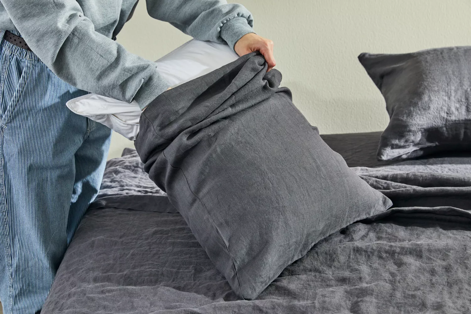  Person putting a pillow in the Quince European Linen pillow cover on a bed during testing