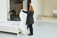 Person holding a white Boll & Branch Signature Hemmed Sheet Set while standing next to bed