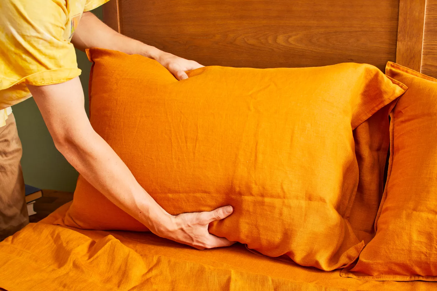 A person places a pillow on a bed made using the Everly Hemp Sheet Set