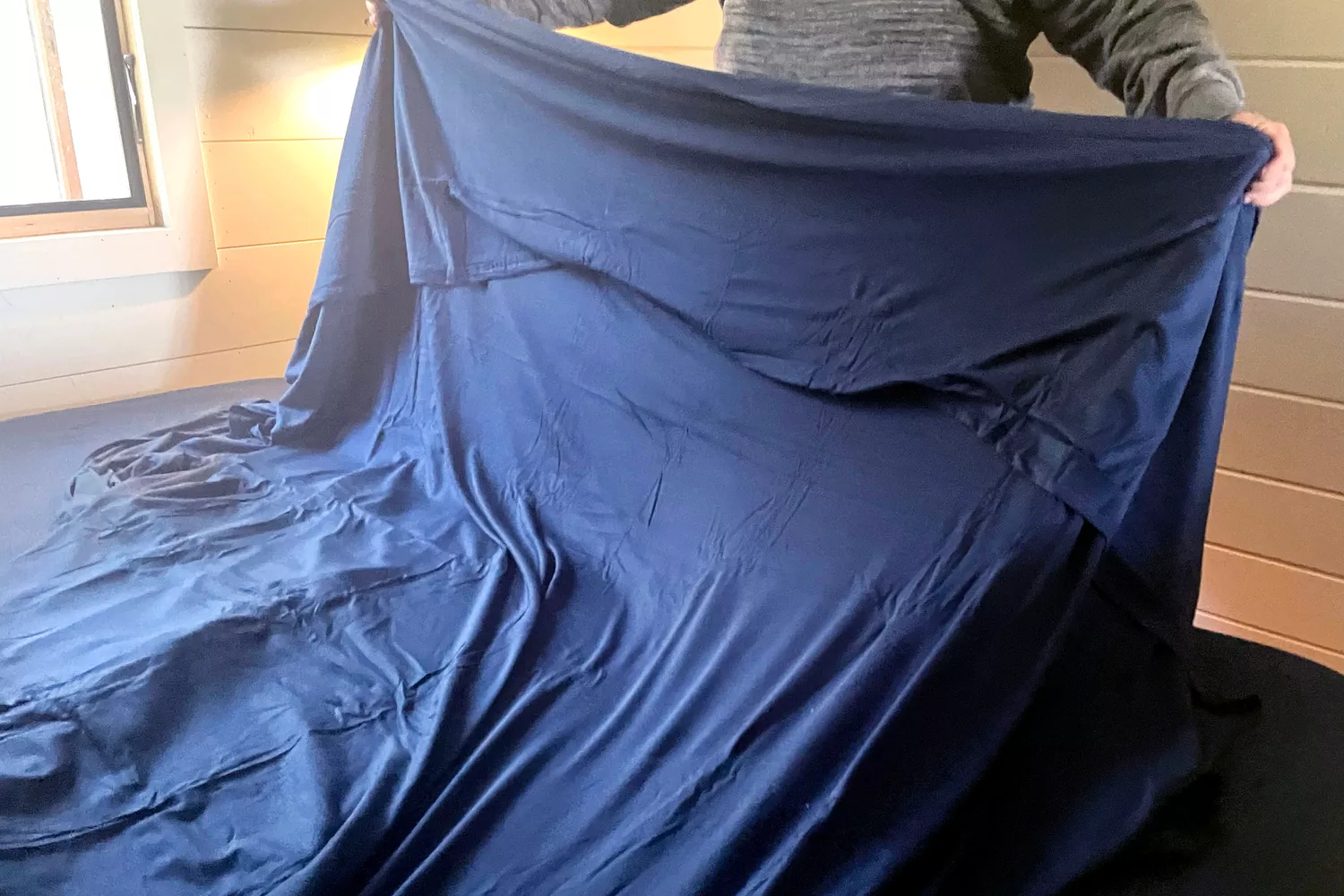 A person makes a bed using the Better Homes & Gardens 4-Piece Jersey Sheet Set